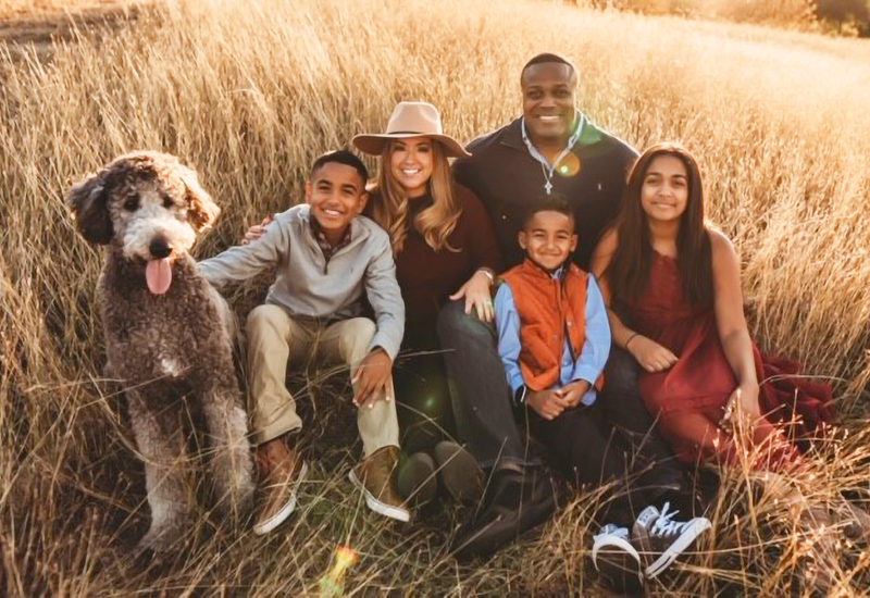 Family portrait of the Reddings sitting and smiling a wheat field with their children and dog.
